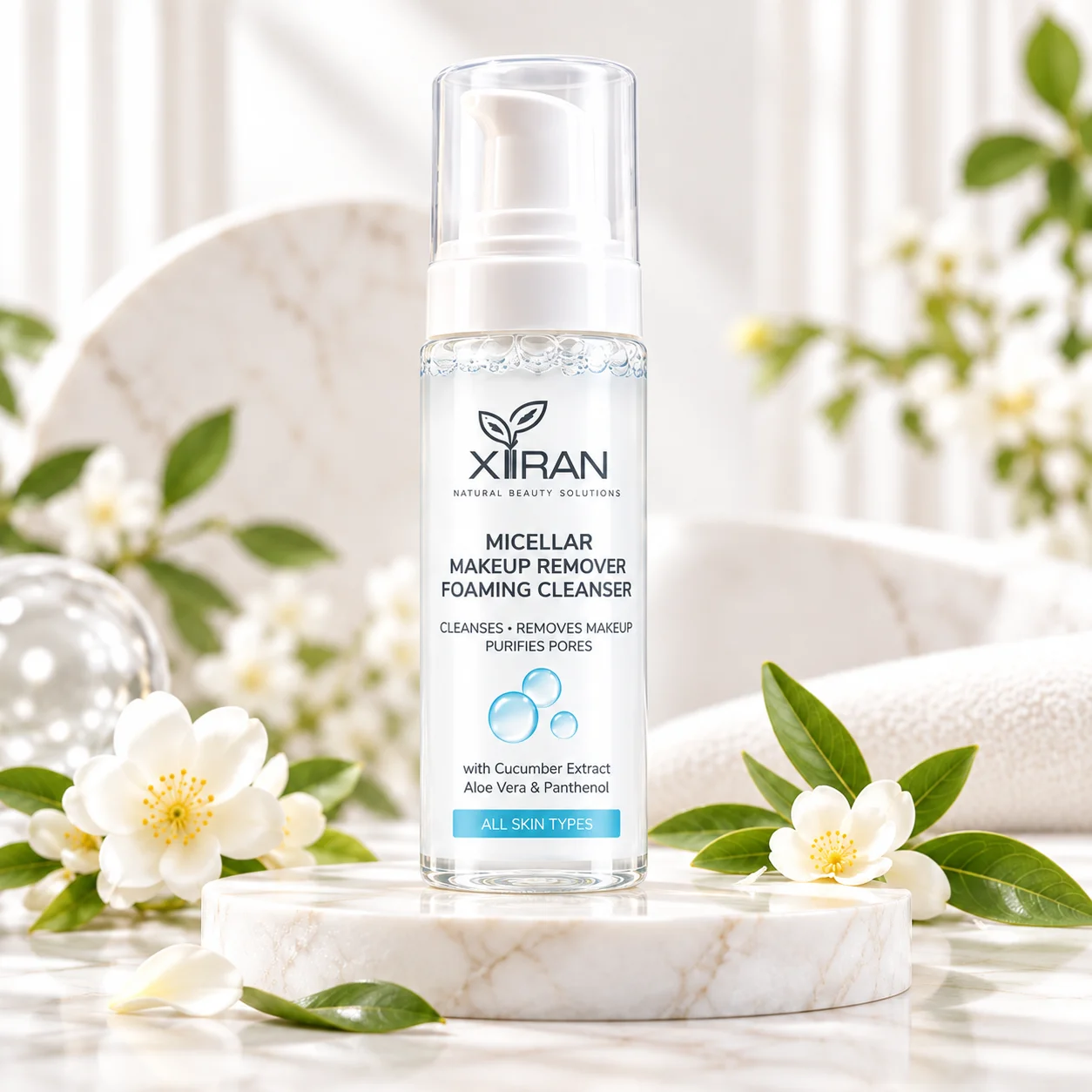 Xiran Micellar Makeup Remover Foaming Cleanser bottle displayed on a marble surface adorned with white flowers and greenery in a bright, elegant setting.